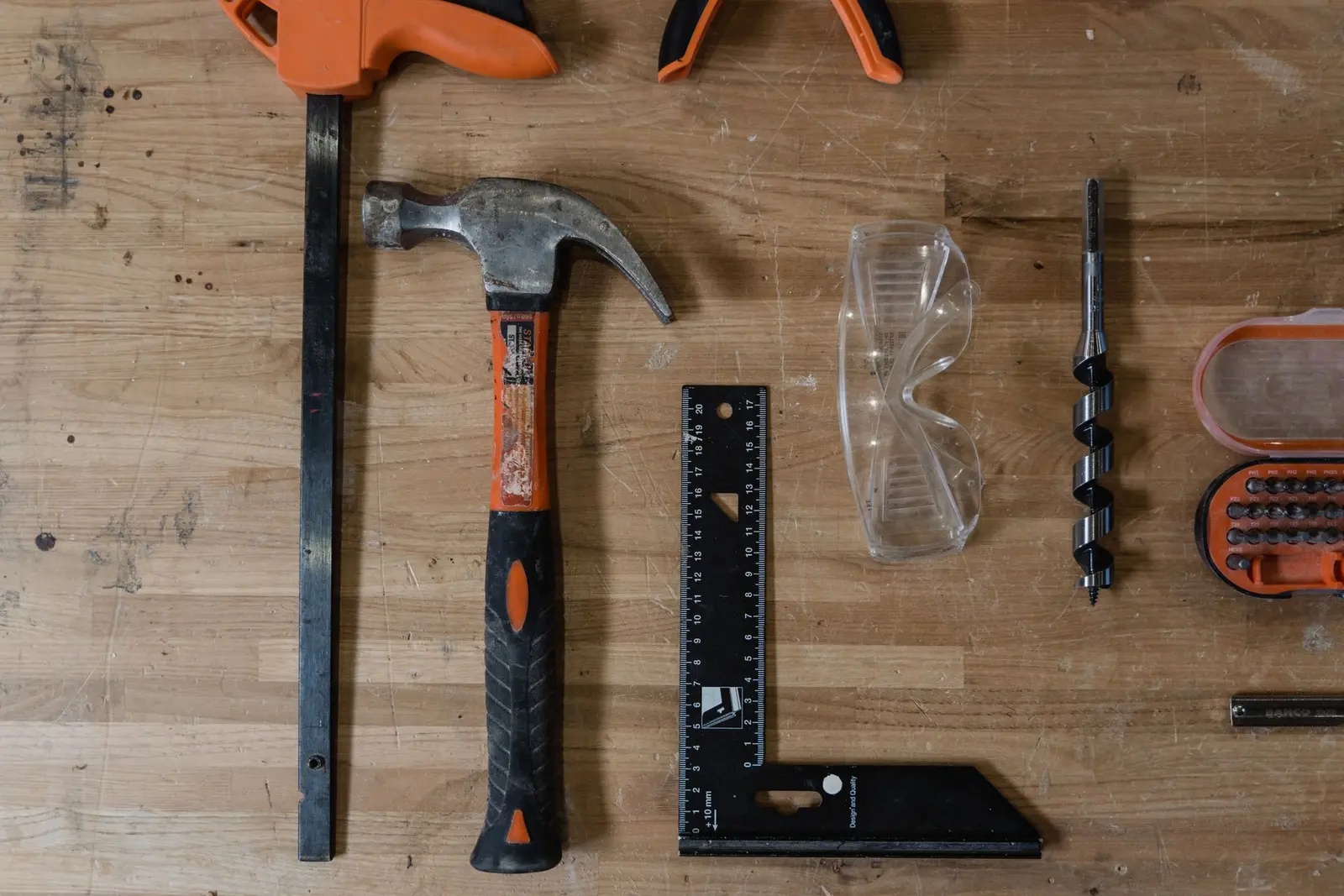 Hammer, vinkel, tvinge og vernebriller på en arbeidsbenk